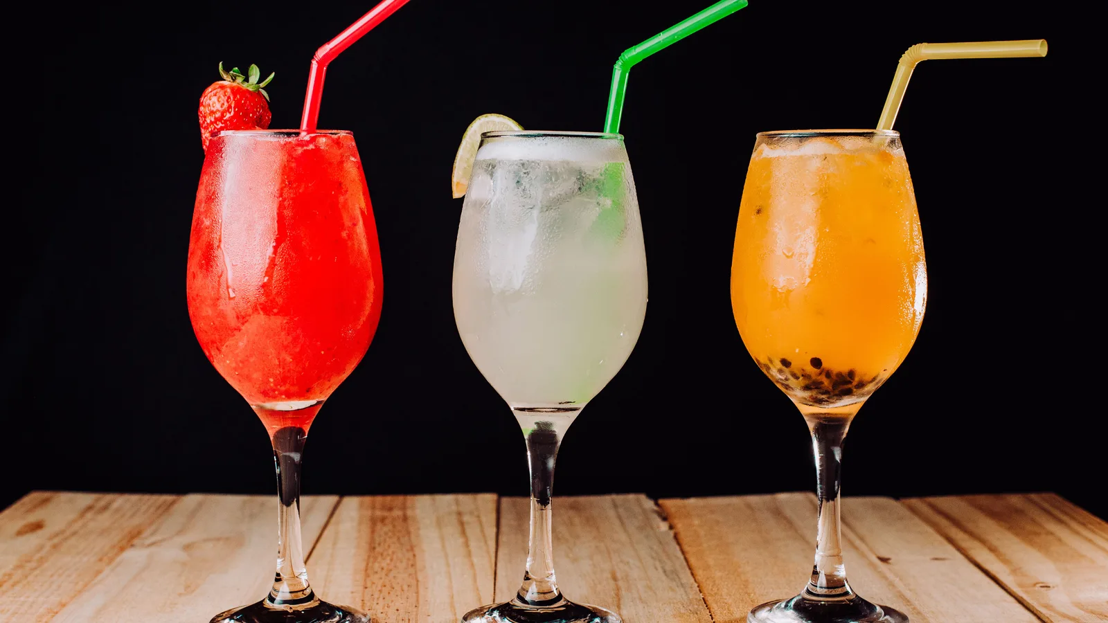 Coquetéis vibrantes com canudos em uma mesa de madeira, perfeitos para um tema de bebida refrescante.