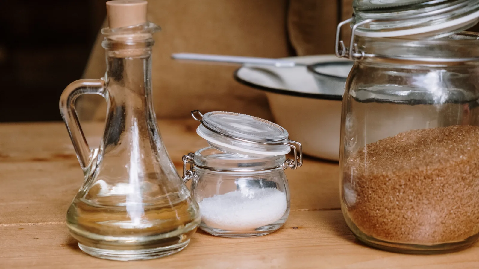 Ingredientes de cozinha variados em frascos de vidro sobre uma bancada de madeira.
