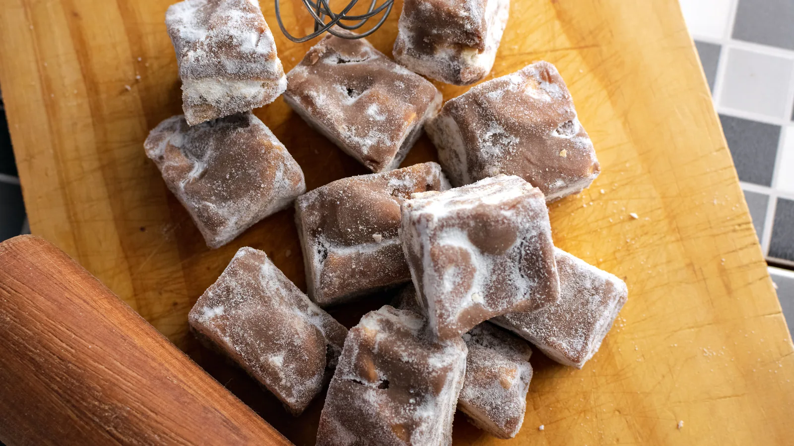 Vista de cima de doces de chocolate caseiros polvilhados com açúcar de confeiteiro em uma tábua de madeira.